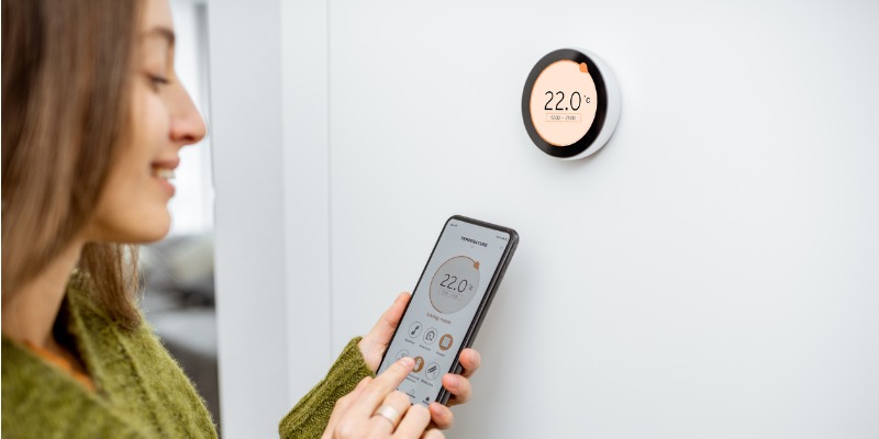 Lady adjusting temp on phone infront of smart thermostat